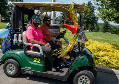 A Prestige Birthday Golf Cart decorated in party decorations driven by two men in pink shirts.