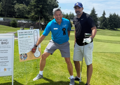 Ravi and Rod point to a graphic depicting fundraising goals while on the green